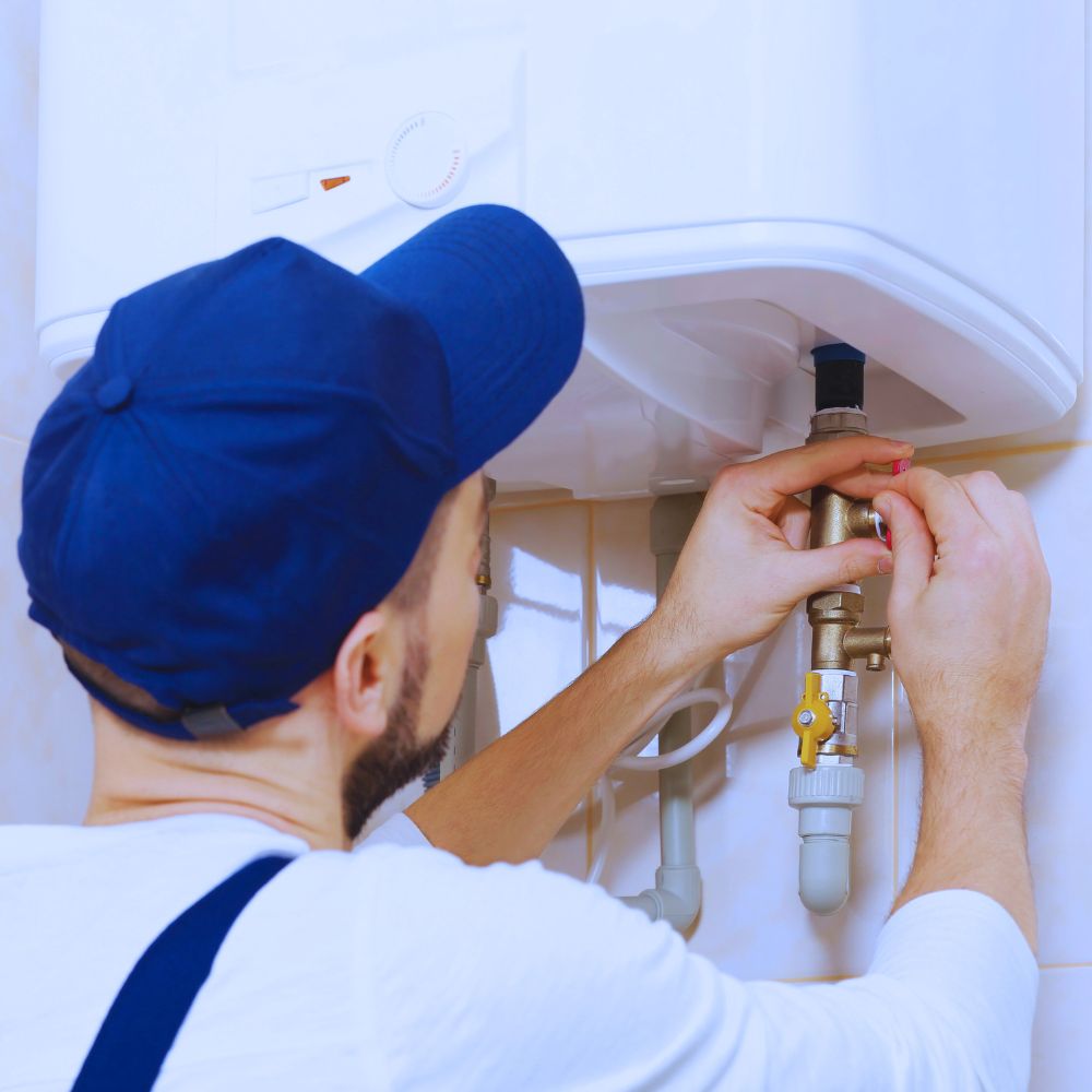 Technicien portant une casquette bleue et ajustant une vanne sur une chaudière murale dans une salle de bain.
